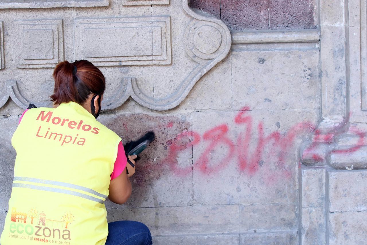 Una trabajadora del área de intendencia del Palacio de Gobierno de Morelos limpia con thinner pintas en la pared